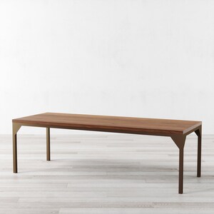 May include: A long, rectangular wooden table with a brown wood top and a gold metal frame. The table has a simple, modern design and would be a great addition to any dining room or living room.