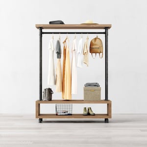May include: A black metal clothing rack with a wooden top and bottom shelf. The rack has a hanging bar with clothes and a backpack hanging from it. The bottom shelf has a wire basket and a pair of brown shoes.