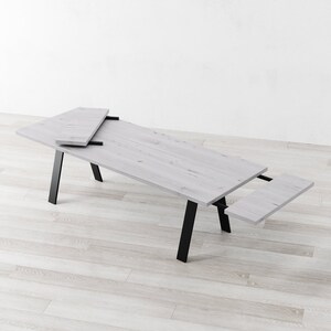 May include: A white wooden dining table with black metal legs. The table has a leaf that can be extended to make it longer.