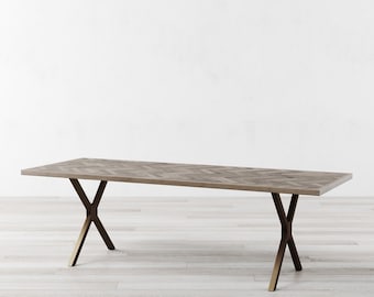May include: A long, rectangular dining table with a light brown wood top featuring a herringbone pattern. The table has a gold metal base with an X-shaped design.