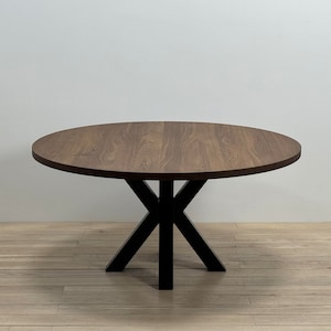 May include: A round wooden dining table with a brown wood top and a black X-shaped base.
