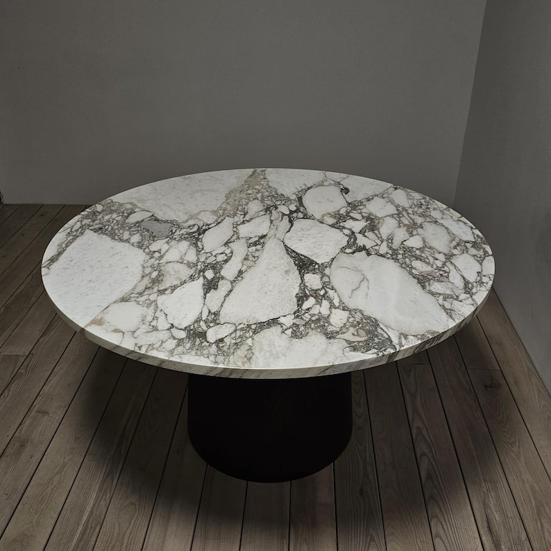May include: A round marble table with a white and grey veined top and a black pedestal base.
