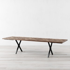 May include: A long, rectangular wooden dining table with a chevron pattern top and black metal X-shaped legs.