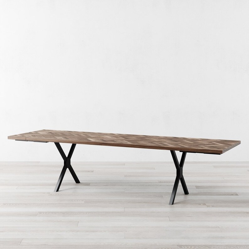 May include: A long, rectangular wooden dining table with a chevron pattern top and black metal X-shaped legs.
