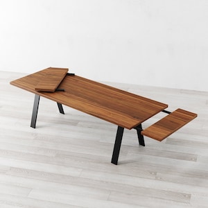 May include: A wooden dining table with black metal legs and two leaf extensions. The table is made of a rich brown wood and has a natural wood finish.