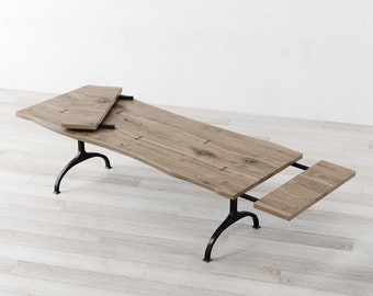 Op de afbeelding: Een houten eettafel met een tafelblad met een levende rand en zwarte metalen poten. De tafel heeft twee bladen die kunnen worden toegevoegd om de lengte van de tafel te vergroten.