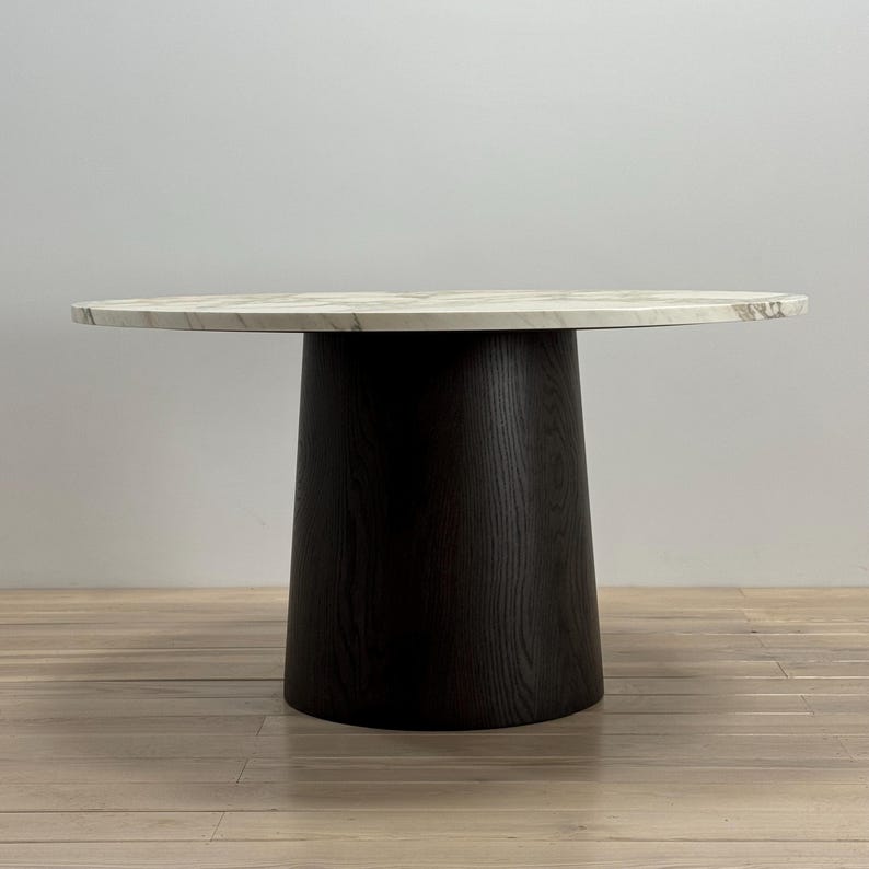 May include: A round, white marble dining table with a black wood base. The table has a smooth, polished surface and a simple, modern design.