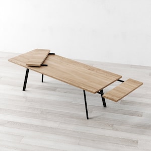 May include: A wooden table with black metal legs and two extendable leaves. The table is made of light wood and has a natural finish.