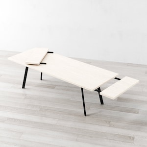 Puede incluir: Una mesa de madera blanca con patas de metal negro. La mesa tiene dos extensiones que se pueden sacar para hacerla más larga.