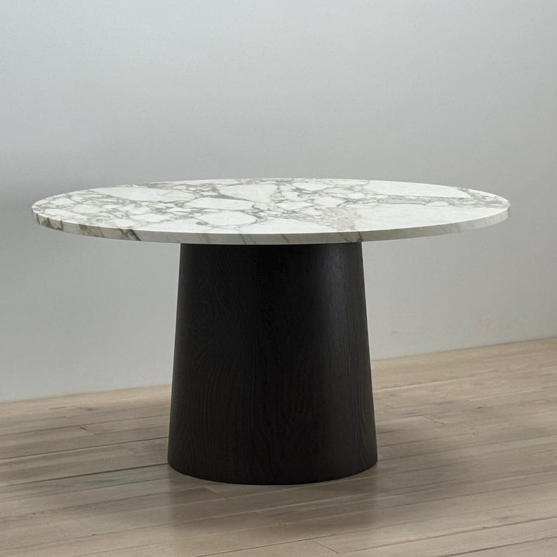 May include: A round white marble table top with a black wood base. The table has a contemporary design and is perfect for a dining room or living room.