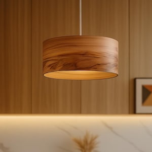 Puede incluir: Una lámpara colgante de madera cuelga sobre una mesa redonda de madera preparada para el té. La cocina cuenta con armarios de madera, una encimera negra y una placa para salpicaduras de mármol. Una tetera, un cuenco y un vaso de té están sobre la mesa.