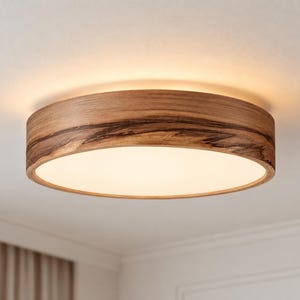 May include: A circular flush mount ceiling light featuring a natural wood grain frame with dark brown streaks and a smooth, white, translucent center panel that emits a warm, soft glow when illuminated against a plain white ceiling surface.