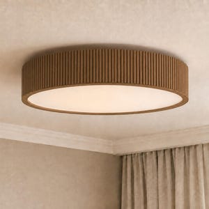 May include: A circular flush mount ceiling light fixture featuring a brown wooden exterior with a vertical slatted design and a flat, opaque white diffuser panel centered on the bottom, mounted directly against a light-colored ceiling surface.