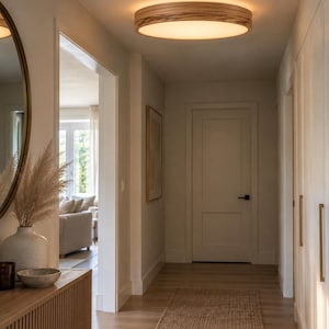 May include: A round flush mount ceiling light fixture featuring a natural wood grain frame and a frosted white diffuser. The light emits a warm glow, illuminating the hallway ceiling with a circular design that integrates into the interior space.