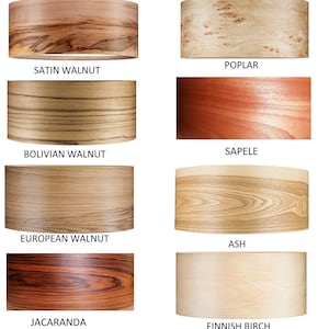 May include: Eight cylindrical drum lampshades featuring distinct wood grain patterns labeled Satin Walnut, Poplar, Bolivian Walnut, Sapele, European Walnut, Ash, Jacaranda, and Finnish Birch, showcasing various natural wood tones and textures.
