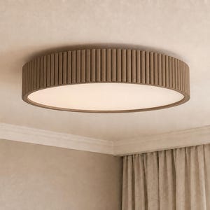 May include: A circular flush mount ceiling light fixture featuring a textured, ribbed brown outer frame and a flat, opaque white diffuser panel that emits a soft, even glow across the surface of the light fixture when illuminated.