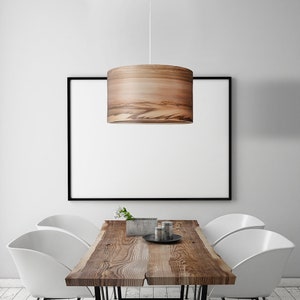 Puede incluir: Una l&aacute;mpara colgante de madera con un acabado de veta de madera natural cuelga sobre una mesa de madera con cuatro sillas blancas. La mesa tiene un dise&ntilde;o de borde vivo y est&aacute; hecha de madera recuperada.