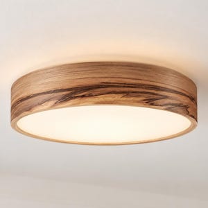 May include: A circular flush mount ceiling light fixture featuring a natural wood grain frame with dark, organic streaks and a smooth, white, translucent center panel that emits a soft, diffused light across the surrounding area.