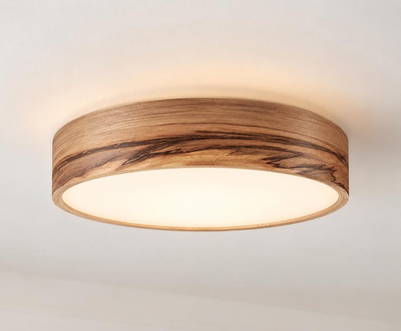 May include: A circular flush mount ceiling light fixture featuring a natural wood grain frame with dark, organic streaks and a smooth, white, translucent center panel that emits a soft, diffused light across the surrounding area.