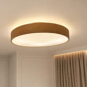 May include: A circular flush mount ceiling light fixture featuring a light brown wood grain frame and a flat, white circular diffuser that emits a soft, warm glow across the ceiling surface, creating a clean and simple lighting solution.