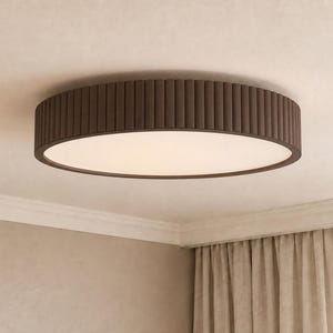 May include: A circular flush mount ceiling light fixture featuring a dark brown exterior frame with a vertical ribbed texture and a flat, circular white diffuser panel that emits a soft, even glow across the surface of the light fixture.