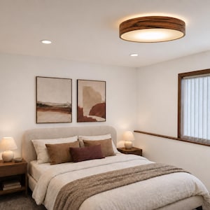 May include: A round ceiling light fixture with a dark wood grain frame and a white diffuser, emitting a warm glow. The light is mounted on a white ceiling above a bed with beige bedding, brown pillows, and two matching bedside lamps.