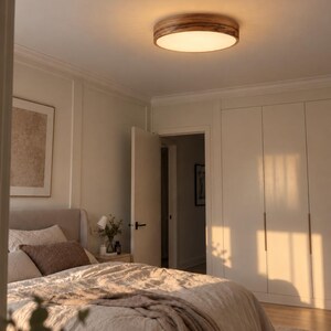 May include: A round flush mount ceiling light fixture featuring a circular wooden frame with a visible grain pattern and a frosted white acrylic diffuser that emits a warm, soft glow, illuminating the bedroom space from above.