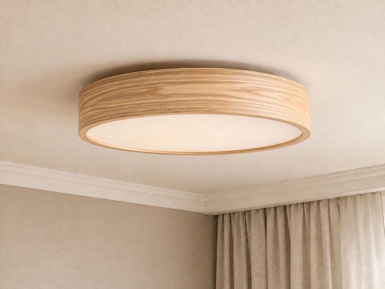 May include: A circular flush mount ceiling light fixture featuring a light-toned wood grain frame and a flat, opaque white diffuser panel that emits a soft, even glow across the surface of the light fixture when illuminated.