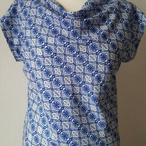 May include: A white and blue patterned blouse with a cowl neck and short sleeves.