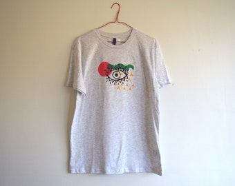 May include: A gray t-shirt with a colorful eye graphic. The eye is surrounded by a red circle, green leaves, and yellow triangles.