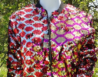May include: A long-sleeve bomber jacket covered in reversible sequins that shift between red, gold, and silver colors. The jacket features a black ribbed collar, black ribbed cuffs, and a black ribbed hem, with a central front zipper closure.