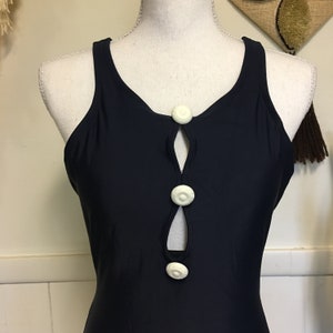 May include: A black swimsuit with a keyhole opening in the front and three white buttons. The swimsuit has a racerback style.