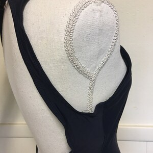 May include: A black swimsuit with a low back and a racerback style. The swimsuit has a simple design and is made of a smooth, stretchy fabric.