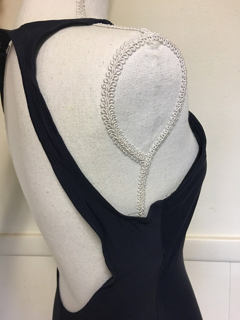 May include: A black swimsuit with a low back and a racerback style. The swimsuit has a simple design and is made of a smooth, stretchy fabric.