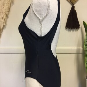 May include: A navy blue one-piece swimsuit with a racerback style and a white "Daniela R" logo on the side.
