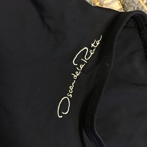May include: A black garment with the text "Oscar de la Renta" embroidered in white on the front.