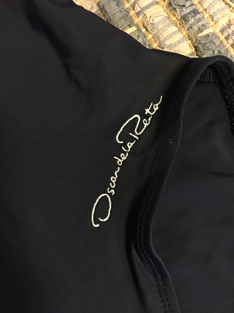 May include: A black garment with the text "Oscar de la Renta" embroidered in white on the front.