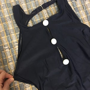 May include: A navy blue swimsuit with a keyhole back and white button accents.