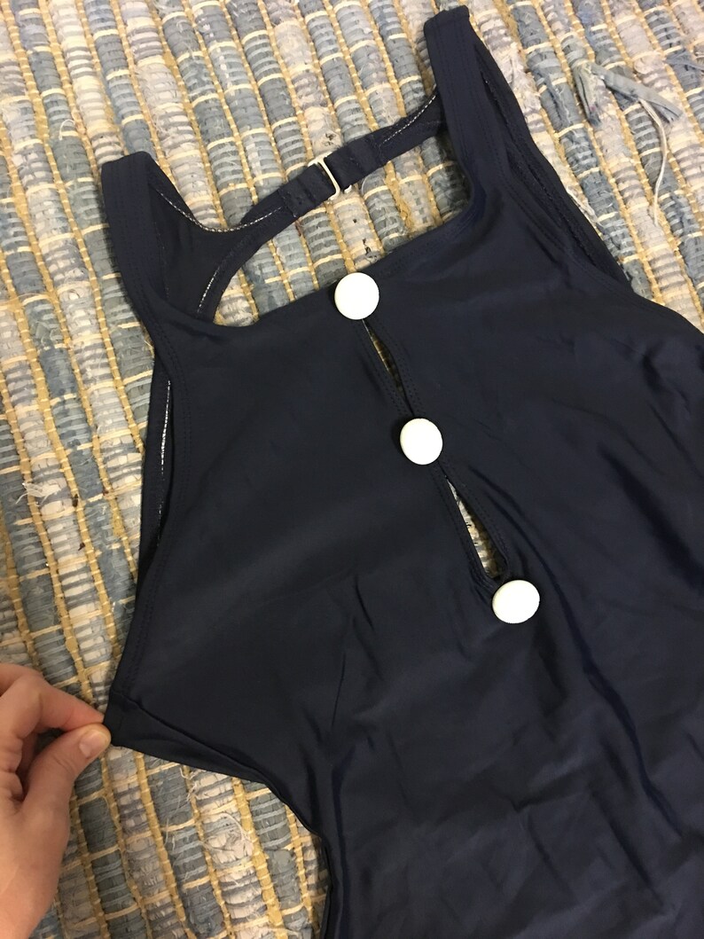 May include: A navy blue swimsuit with a keyhole back and white button accents.