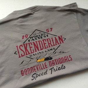 May include: Gray t-shirt with a red and white graphic design. The graphic features a vintage-style logo with the text "19 57 Officially World's Fastest Iskenderian Racing Cams" and "Bonneville Nationals Speed Trials".