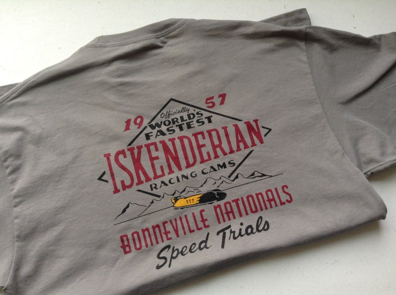 May include: Gray t-shirt with a red and white graphic design. The graphic features a vintage-style logo with the text "19 57 Officially World's Fastest Iskenderian Racing Cams" and "Bonneville Nationals Speed Trials".