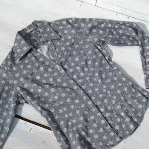 Puede incluir: Una camisa gris de manga larga con botones y un estampado floral blanco.