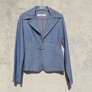 Può includere: Un blazer in denim blu con fodera rossa e chiusura con un solo bottone. Il blazer ha una silhouette aderente e maniche lunghe.