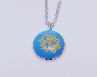 May include: A silver chain necklace with a round pendant featuring a pressed flower encased in blue resin.