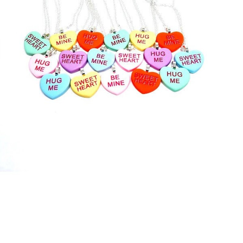 Op de afbeelding: Een verzameling van 15 zilveren kettingen met hartvormige hangers. De hangers zijn in verschillende kleuren en hebben verschillende berichten, waaronder "Sweet Heart", "Hug Me", "Be Mine" en "Sweet Heart".
