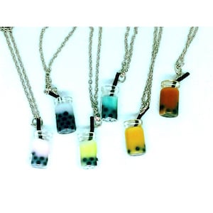 May include: Six silver necklaces with miniature glass bottles filled with different colored bubble tea. The bottles have black straws and are attached to the silver chains.