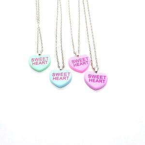 Op de afbeelding: Vier zilveren kettingen met hartvormige hangers. De hangers zijn in roze en blauwe tinten en zeggen "Sweet Heart" erop.