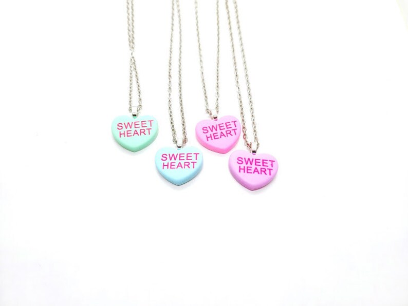 Op de afbeelding: Vier zilveren kettingen met hartvormige hangers. De hangers zijn in roze en blauwe tinten en zeggen "Sweet Heart" erop.