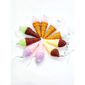 Op de afbeelding: Een set van acht ijshoorntjes oorbellen. De oorbellen zijn gemaakt van polymer clay en hebben verschillende smaken ijs, waaronder chocolade, vanille, aardbei en muntchocolade. De oorbellen zijn allemaal zilverkleurig en hebben een haaksluiting.