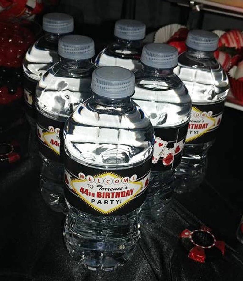 May include: A set of six clear plastic water bottles with black and red labels. The labels have a Las Vegas theme and say "Welcome to Terrence's 44th Birthday Party!"